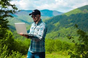 guy smiling and working on laptop in the mountains photo