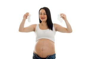 young pregnant brunette woman posing with little white socks in her hands isolated on  background photo