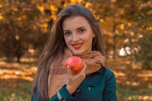 smiling pretty girl stands in the Park and holds a Red Apple in hand photo