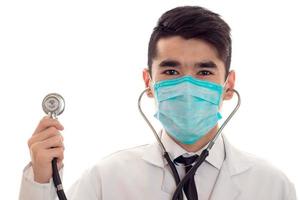 young handsome man doctor posing in uniform and mask with stethoscope isolated on white background in studio photo