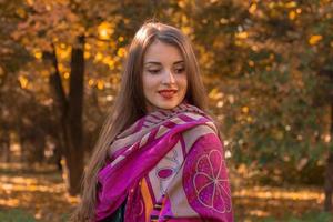 cute young girl stands in the park with a large pink scarf on the shoulders and looks away photo