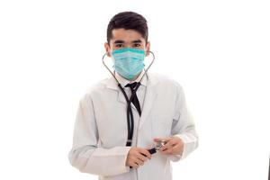 young male doctor in uniform and mask with stethoscope looking at the camera isolated on white background photo