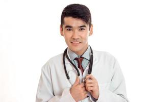 joven médico de uniforme con estatoscopio mirando a la cámara y sonriendo aislado de fondo blanco foto