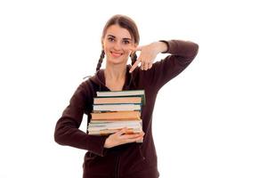 feliz joven estudiante morena con ropa deportiva marrón con un montón de libros en las manos sonriendo a la cámara aislada de fondo blanco foto