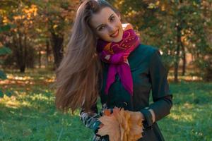 young girl with long straight hair cocked her head smiling and keeps the leaves in the hands of photo