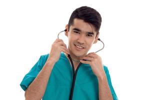 portrait of cheerful young brunette man doctor in blue uniform with stethoscope posing isolated on white background photo