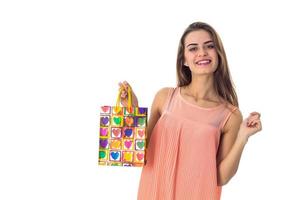una chica alegre se pone de pie y sostiene un paquete de color con un regalo aislado de fondo blanco foto