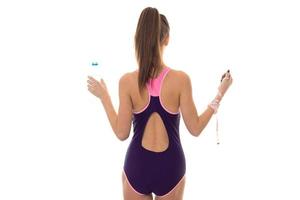 slim young brunette woman in magenta body swimsuit with sexy round butt posing with water bottle nad measure tape isolated on white background photo
