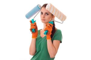 portrait of young tired brunette building woman in uniform with paint roller in hands makes renovation and looking at the camera isolated on white background photo