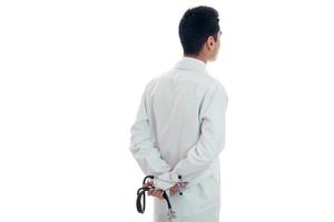 doctor in white gown stands looking backwards and holding a stethoscope isolated on white background photo