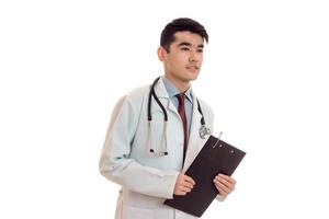 young sexy brunette man doctor in uniform with stethoscope on his shoulders make notes isolated on white background photo