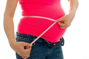 mujer embarazada con camisa rosa brillante mide su vientre con cinta aislada de fondo blanco foto
