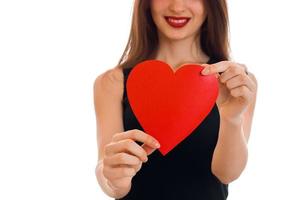 beautiful young girl in black dress holding a card in the shape of a heart and a smiling of isolated on white background photo