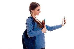 adolescente con coletas mantiene una mochila en la espalda y fotografiada en el teléfono girando de lado a la cámara foto