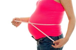 El primer plano de una mujer embarazada mide su vientre con cinta aislada de fondo blanco