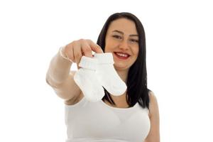 young pregnant brunette girl with little socks in her hands looking and smiling on camera isolated on white background photo