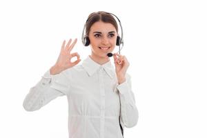 young girl in white shirt and headphones with microphone smiles and shows the hand gesture photo
