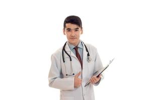 un médico joven con una bata blanca de laboratorio con un estetoscopio mira directamente y mantiene la tableta foto