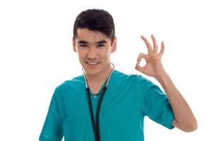 un joven médico vestido de azul con sonrisas de estetoscopio y gesto de mano está aislado en un fondo blanco foto