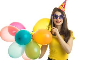 una joven alegre con una blusa amarilla sosteniendo grandes bolas de colores y anteojos artificiales foto