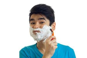 Portrait of a cheerful young man with foam on his face who shaves his beard machine close-up photo