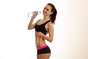 smiling sports girl stands sideways and drinks water from a bottle photo