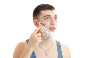 Portrait of a handsome young guy with foam on his face that opened the mouth looks up and shaves his beard