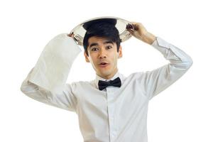 young cheerful waiter in a white shirt to put on his head a tray for Cookware photo