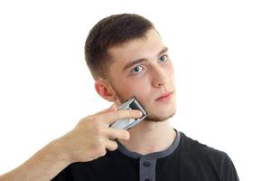 Portrait of attractive young guy who seriously shaves a beard trimmer close-up photo