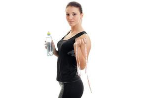 beautiful young girl in black sports suit stands sideways and holding a bottle of water and a measuring tape photo