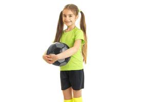 linda niñita con camiseta verde se para en el estudio y sostiene la pelota foto