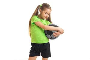 una niña pequeña con una camiseta brillante se para en el estudio y abraza las manos de la pelota foto