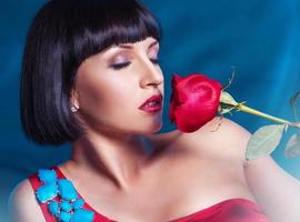Cute brunette with red rose on blue background in studio photo