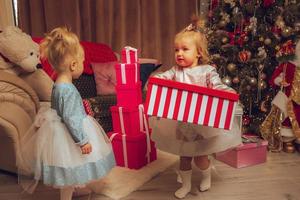 two little baby sisters with a christmas tree from behind at home photo