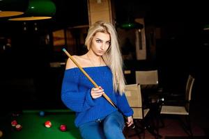 Pretty blonde woman posing with the cue at pool table photo