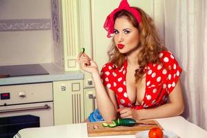 Cutie young sexual woman with curly hair eats cucumber on the kitchen photo