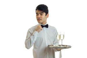 charming handsome young waiter with black hair adjusts his bow tie and hand holding a tray with two glasses photo