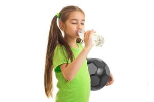 girl in green shirt with soccer ball in hands drinks water photo
