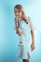 Sweet blonde nurse with stethoscope in white medical gown photo