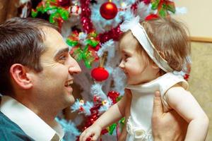 papá con su pequeña hija se miran a los ojos y sonríen en Navidad foto