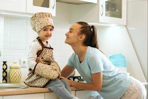 cute little homecook girl with her beautiful mother makes pancakes in white kitchen. photo