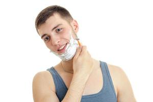 a cheerful young man with foam on his face worth bending head smiling and shaves his beard is isolated on a white background photo
