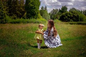 Cheerful mother plays with her little daughter at the green meadow photo