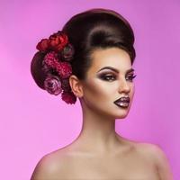 hermosa morena adulta con peinado de maquillaje y flores en el cabello sobre fondo púrpura foto