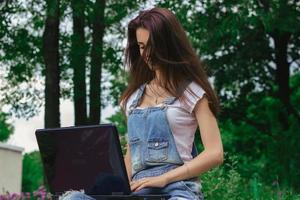 young cute brunette with long hair sitting in a park with a laptop photo