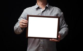 A blank diploma or a mockup certificate in the hand of a man employee wearing a shirt on black background. The horizontal picture frame is empty and the copy space.