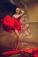 Girl dressed as Santa with a bag of gifts and long sexy legs near the Christmas tree