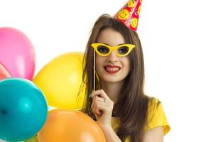 Portrait of a beautiful young girl who smiles and keeps near the face paper glasses with balls photo