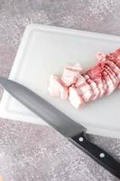 streaky pork is sliced on a white chopping board in the kitchen.Close up cutting slide pork belly raw photo