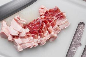 streaky pork is sliced on a white chopping board in the kitchen.Close up cutting slide pork belly raw photo